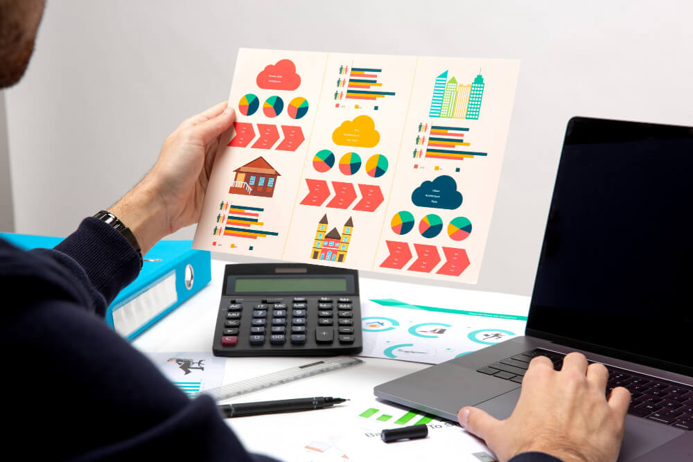 Visão de traz de uma pessoa sentada à mesa do escritorio, analisando mapa com gráficos de vendas